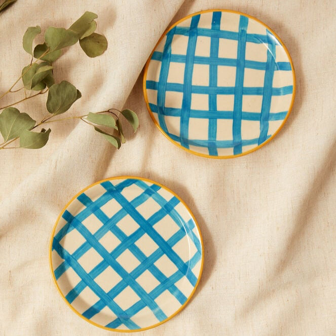 Two ceramic plates with blue grid pattern on a beige fabric background