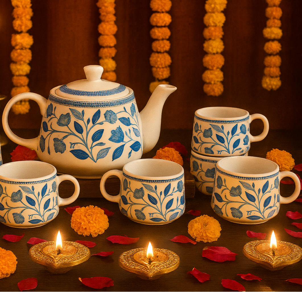 Tea set with teapot and cups on a dark surface with candles and decorative flowers.