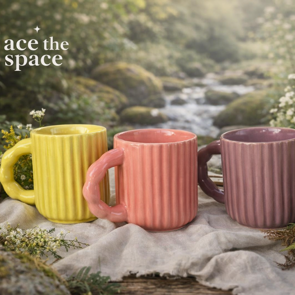 Three colorful mugs (yellow, pink, purple) on a rock with a natural background.