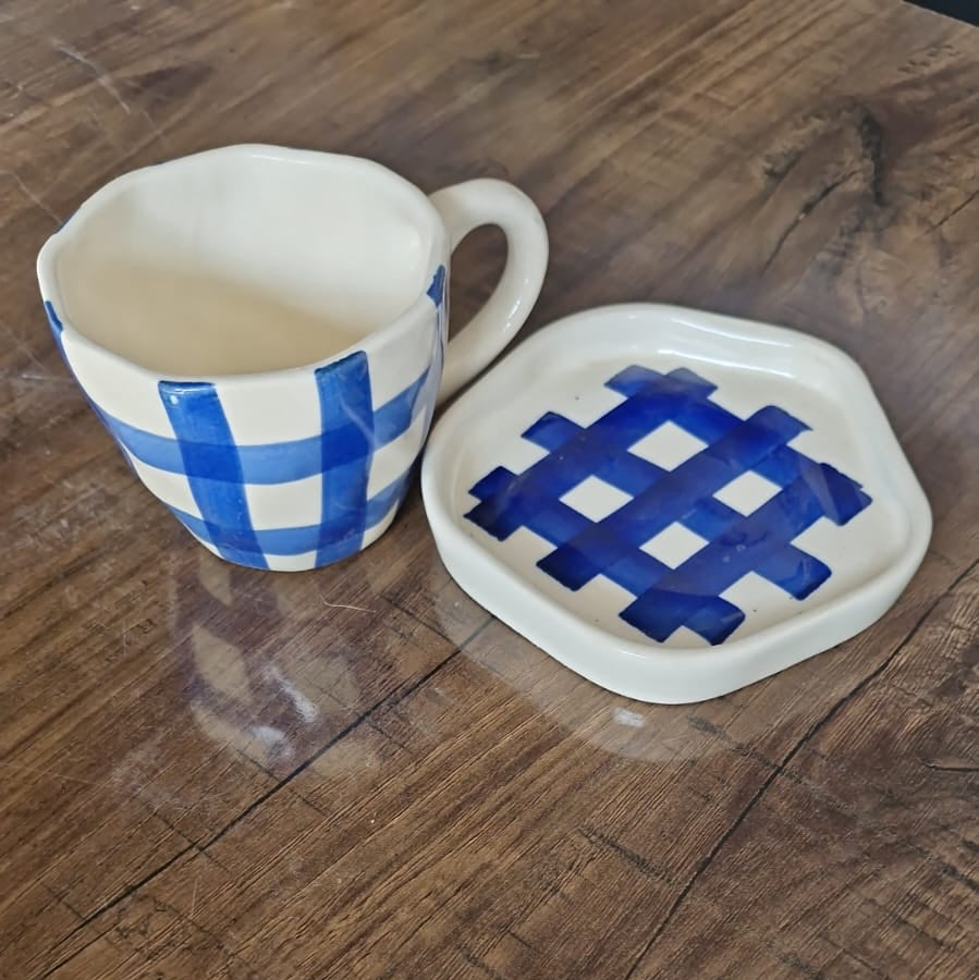 Ceramic mug and coaster with blue and white checkered pattern on a wooden surface