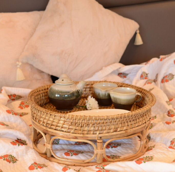 Wicker tray with teacups on a floral blanket with pillows in the background