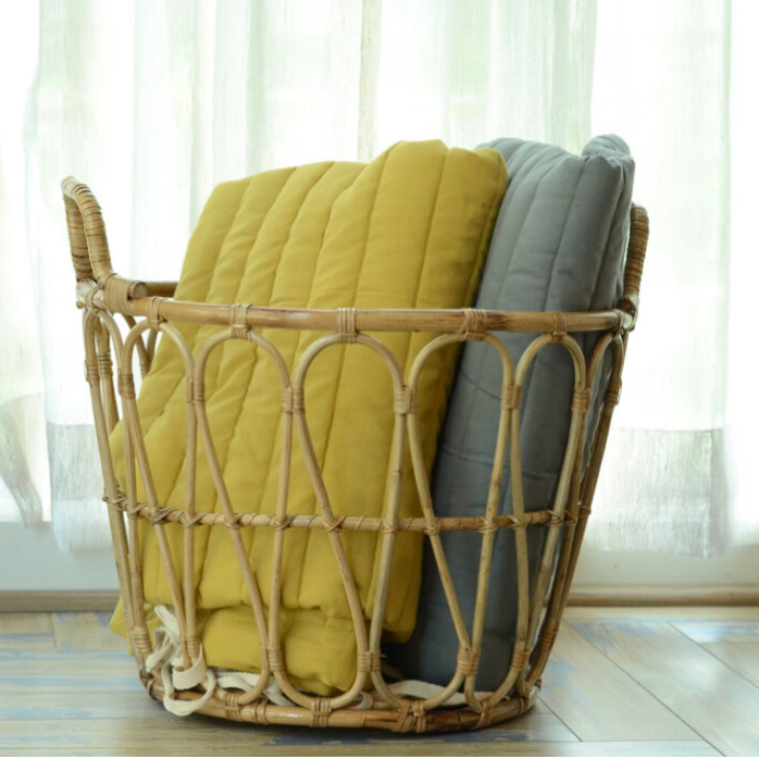 Wicker basket with yellow and gray cushions against a light curtain background