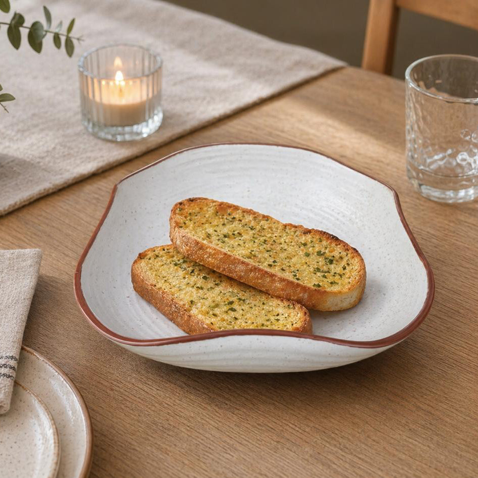 Two slices of garlic bread on a decorative plate with a candle and glass in the background.