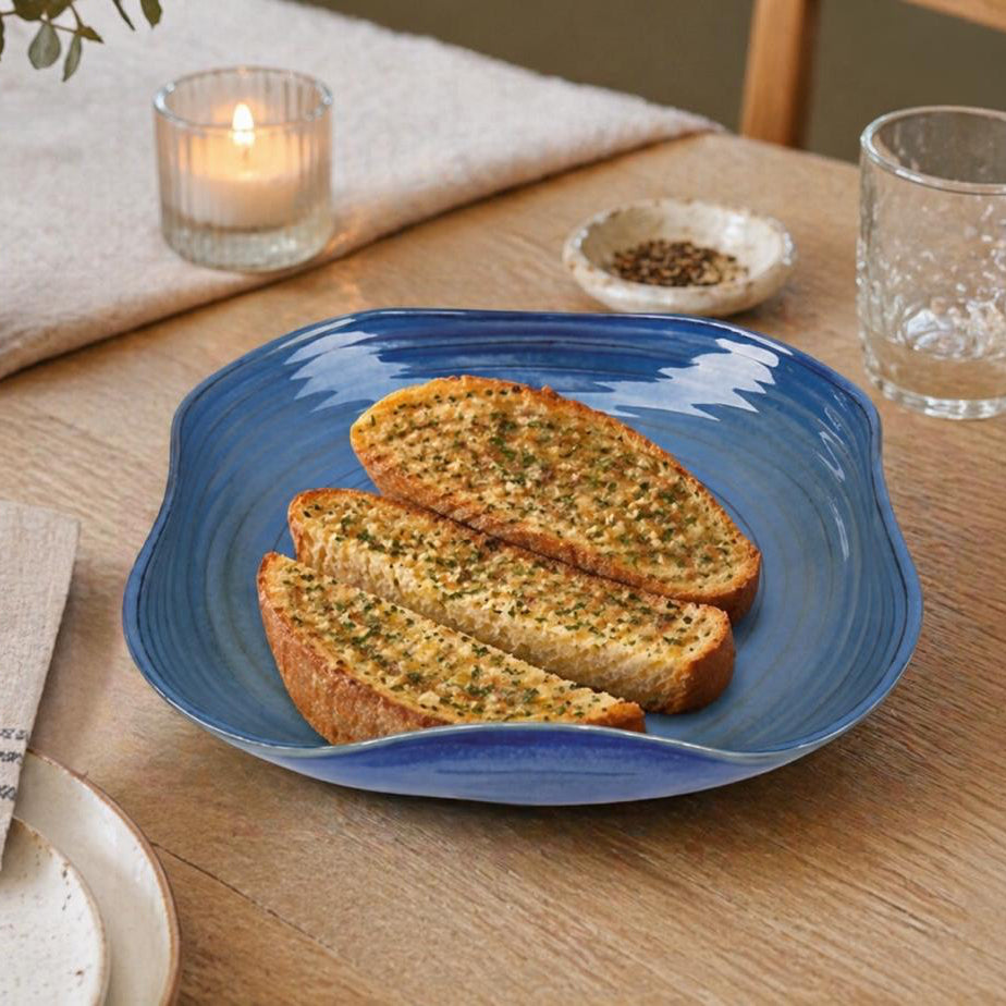 Two pieces of garlic bread on a blue plate with a candle and glass in the background.
