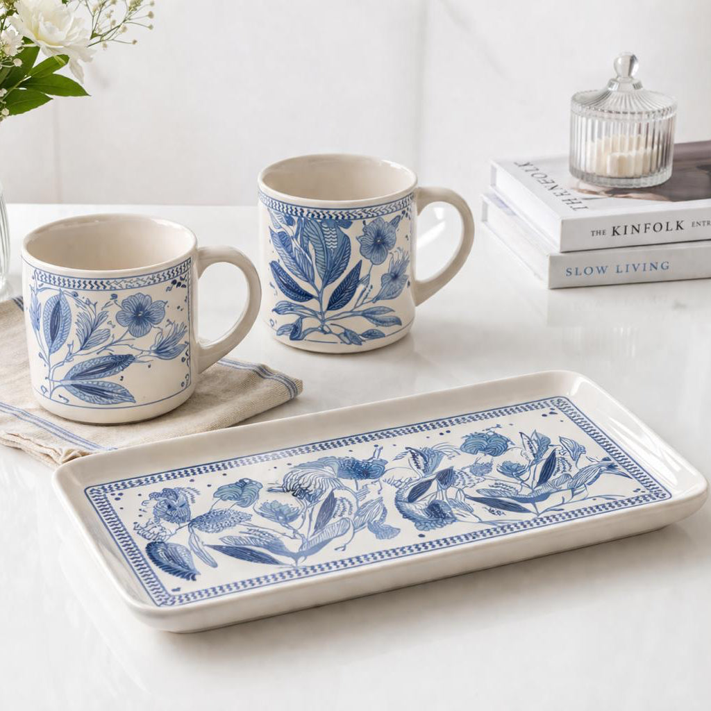 Ceramic mugs and tray with blue floral patterns on a white surface.