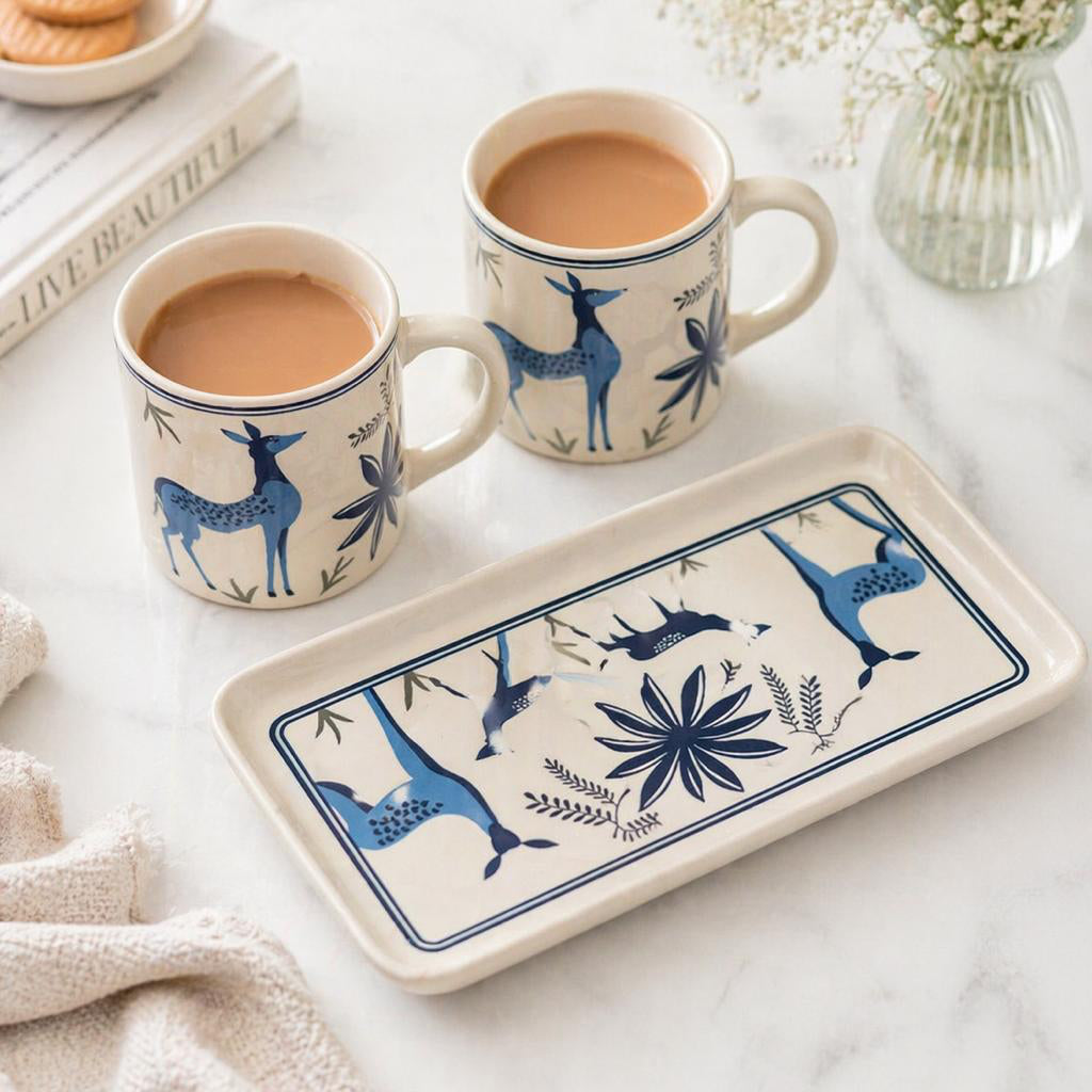 Two mugs with deer design on a tray and cookies on a book