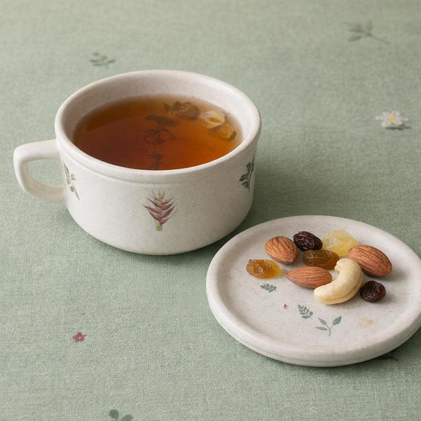 Teacup with tea and a plate of nuts on a green patterned surface