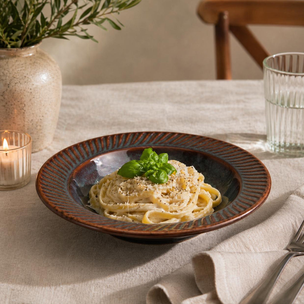 Pasta dish on a table with a candle and glass