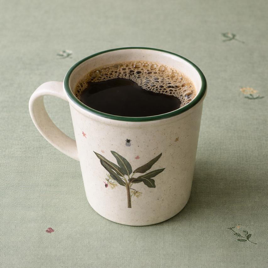 Mug with a botanical design filled with coffee on a textured green surface