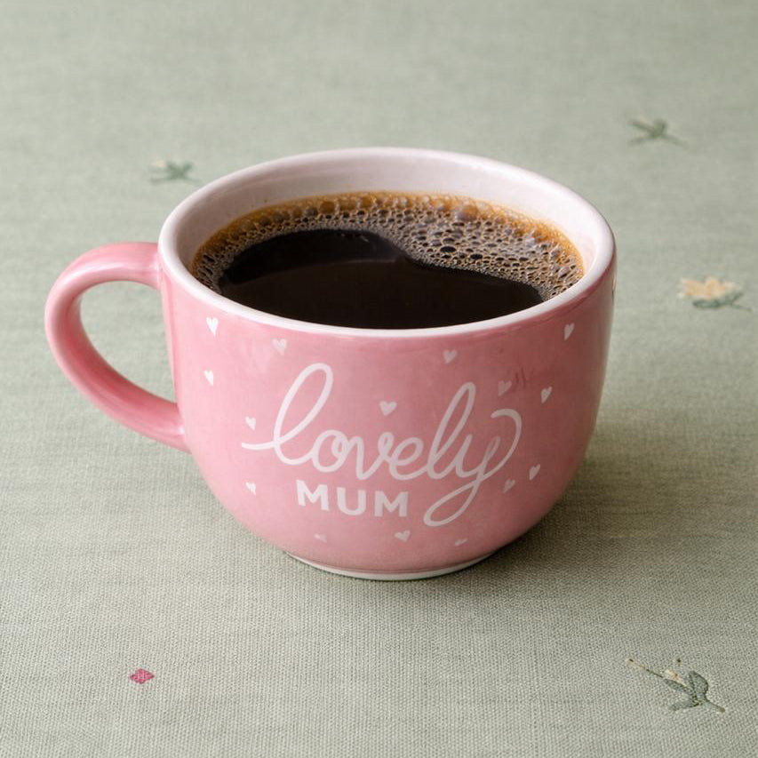 Pink mug with 'lovely mum' text on a light green fabric background