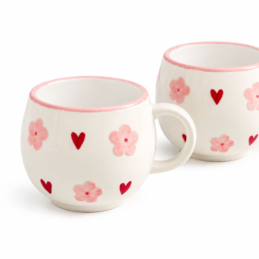 Two ceramic mugs with floral and heart patterns on a white background