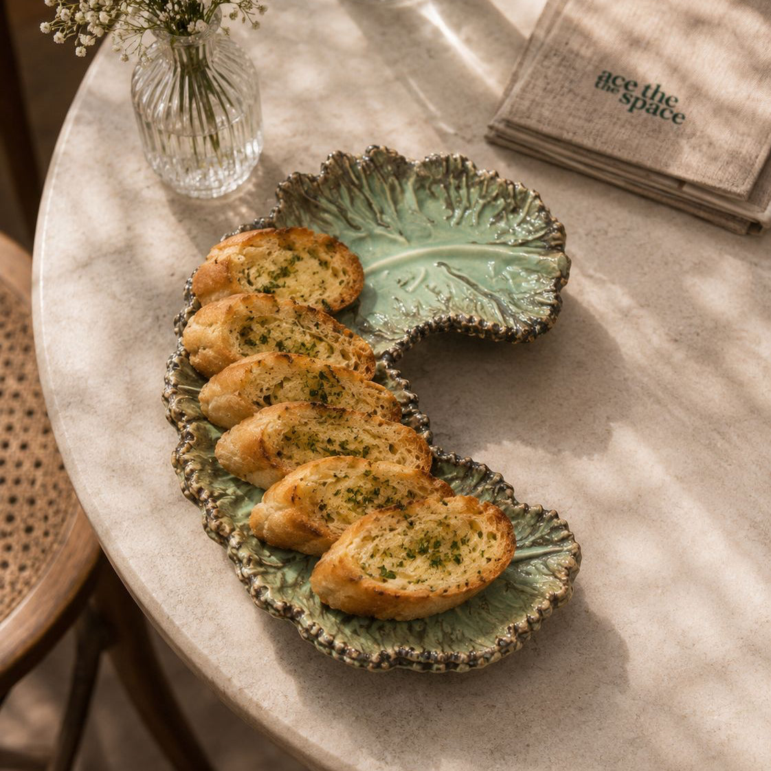 Baked bread on a decorative plate with a vase of flowers and napkins in the background.
