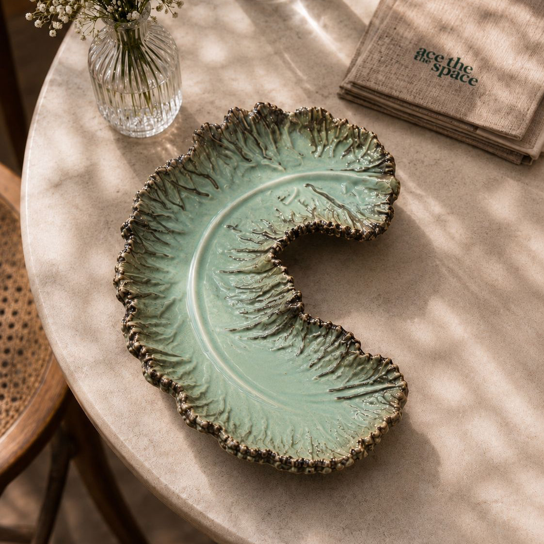 Decorative leaf-shaped ceramic plate on a marble table with a vase and napkins in the background.