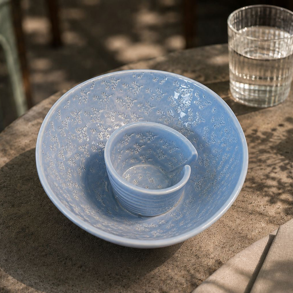 Blue ceramic bowl on a stone surface with a glass of water and small plant in the background.