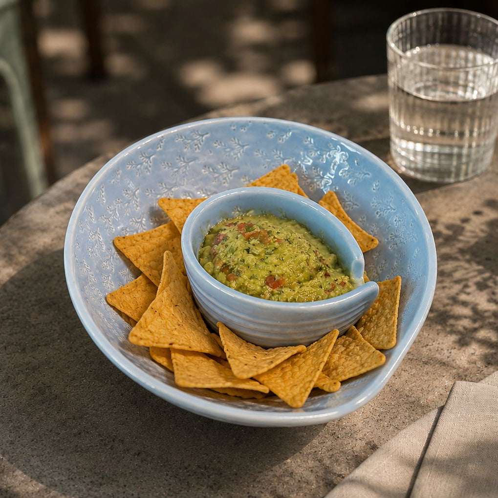 Bowl of guacamole with tortilla chips on a stone table outdoors