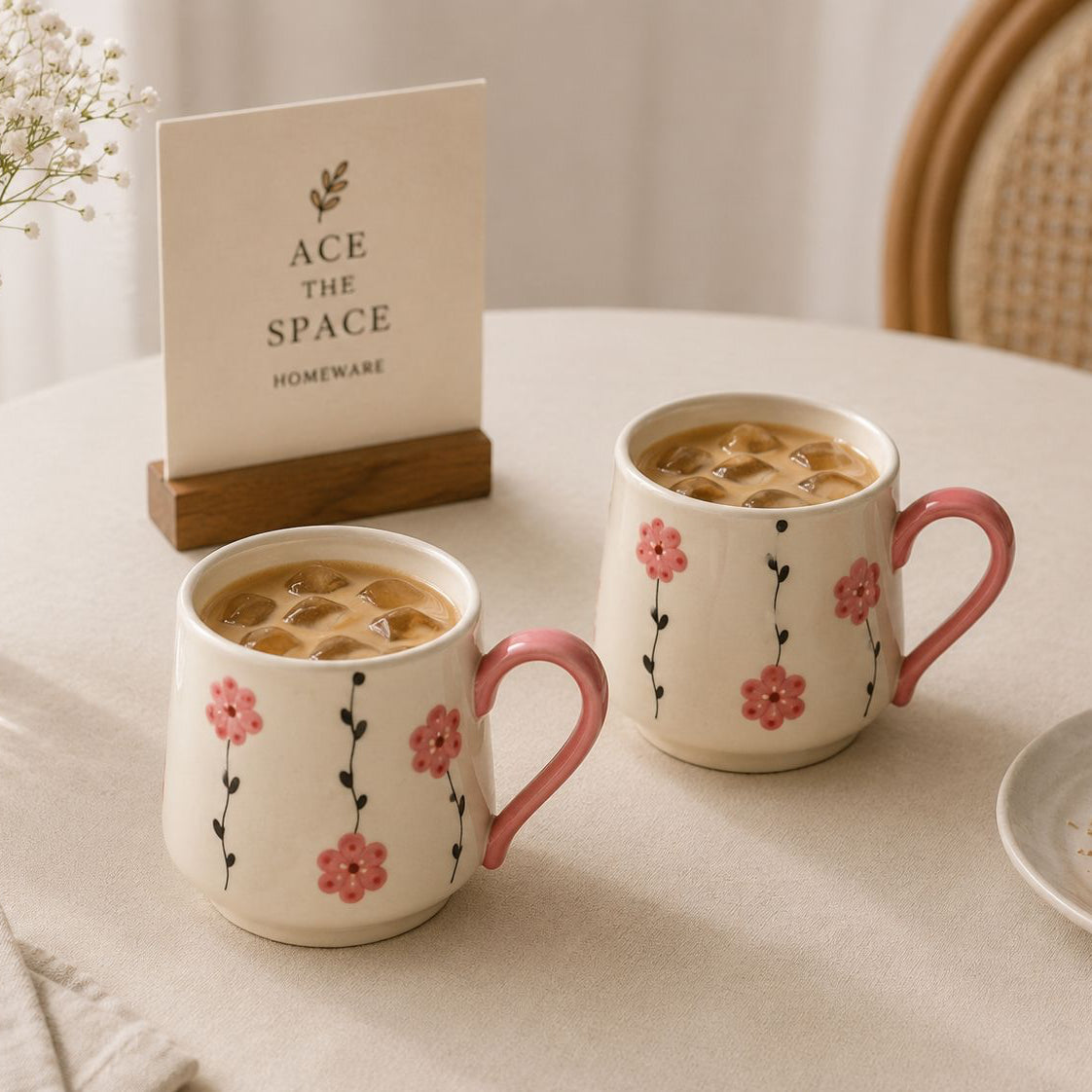Two floral mugs with hot chocolate on a table with a 'ACE THE SPACE' sign in the background.
