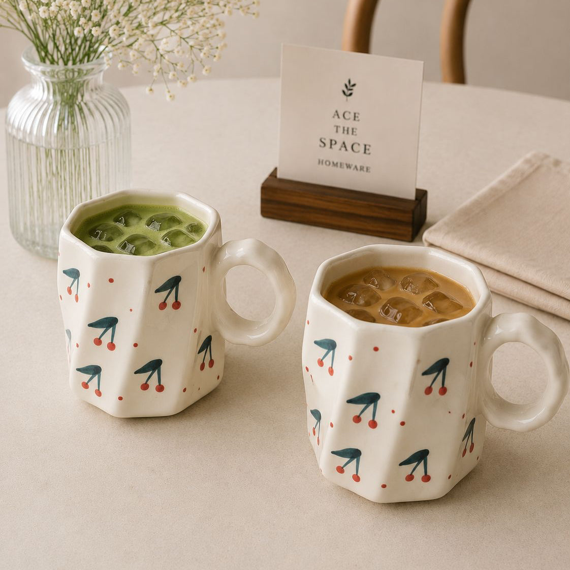 Two mugs with decorative patterns on a table with a card in the background.