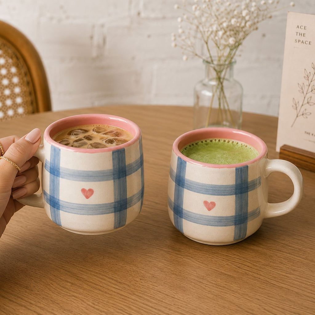 Two ceramic mugs with plaid patterns and heart designs on a wooden table.