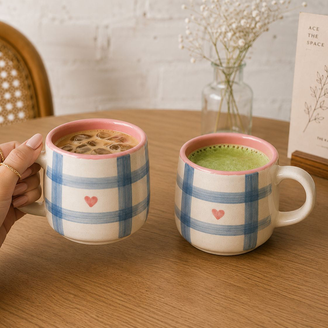 Two ceramic mugs with plaid patterns and heart designs on a wooden table.