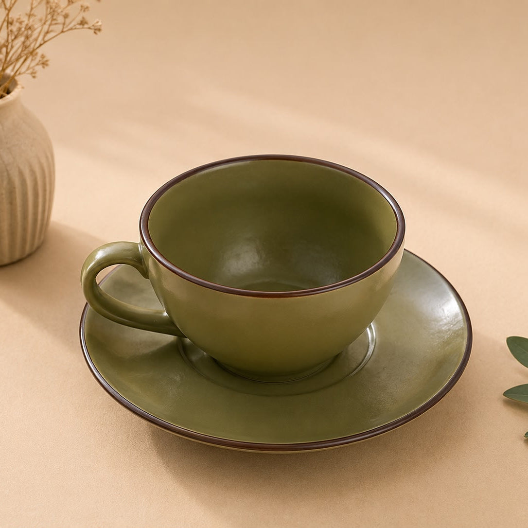 Green ceramic cup and saucer set on a beige surface with a small vase and leaves.
