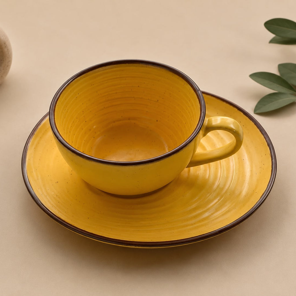 Yellow ceramic cup and saucer on a beige surface with a small plant.