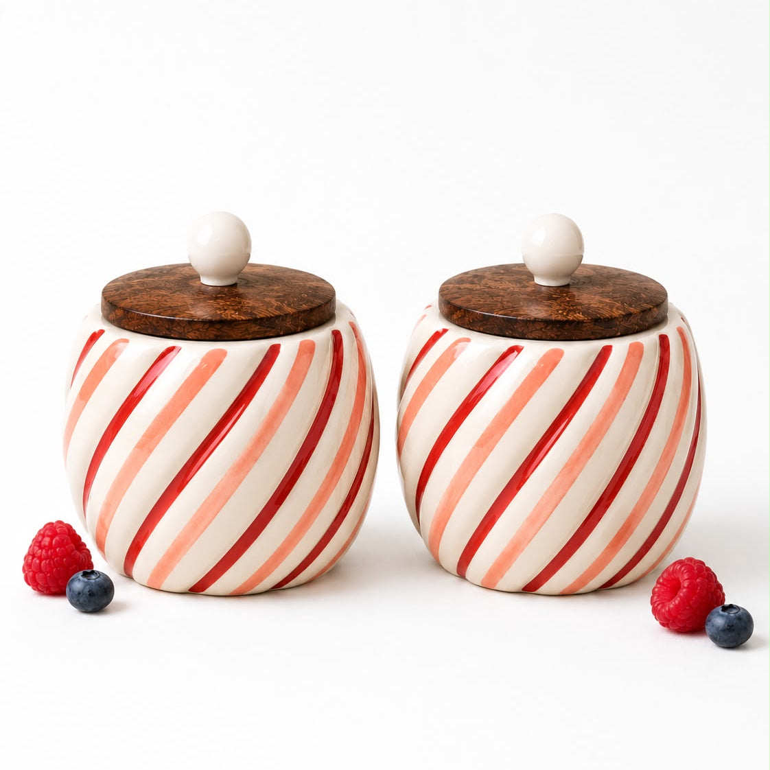 Two striped ceramic jars with wooden lids on a white background with berries.