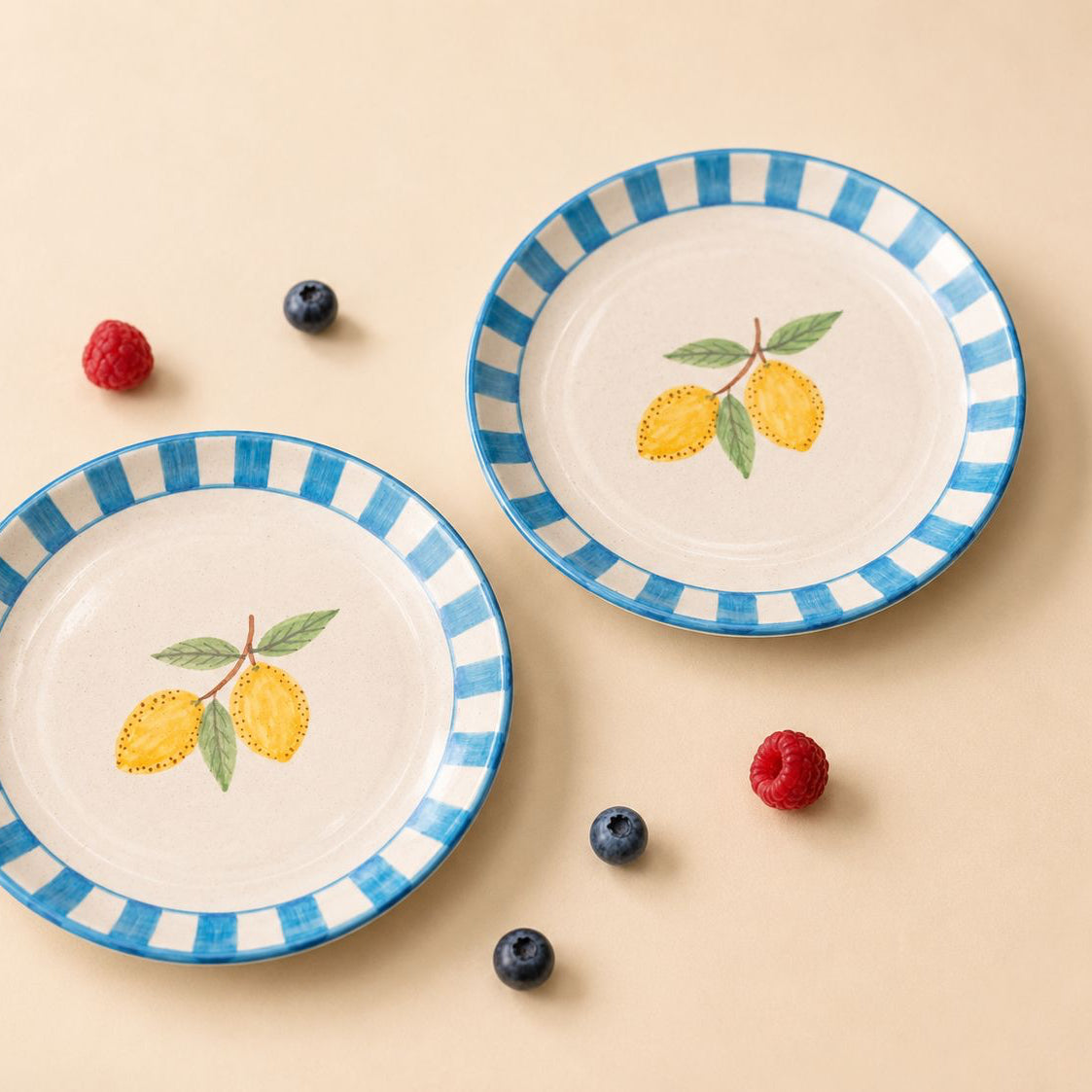 Two ceramic plates with blue and white stripes and lemon design on a beige background with berries.