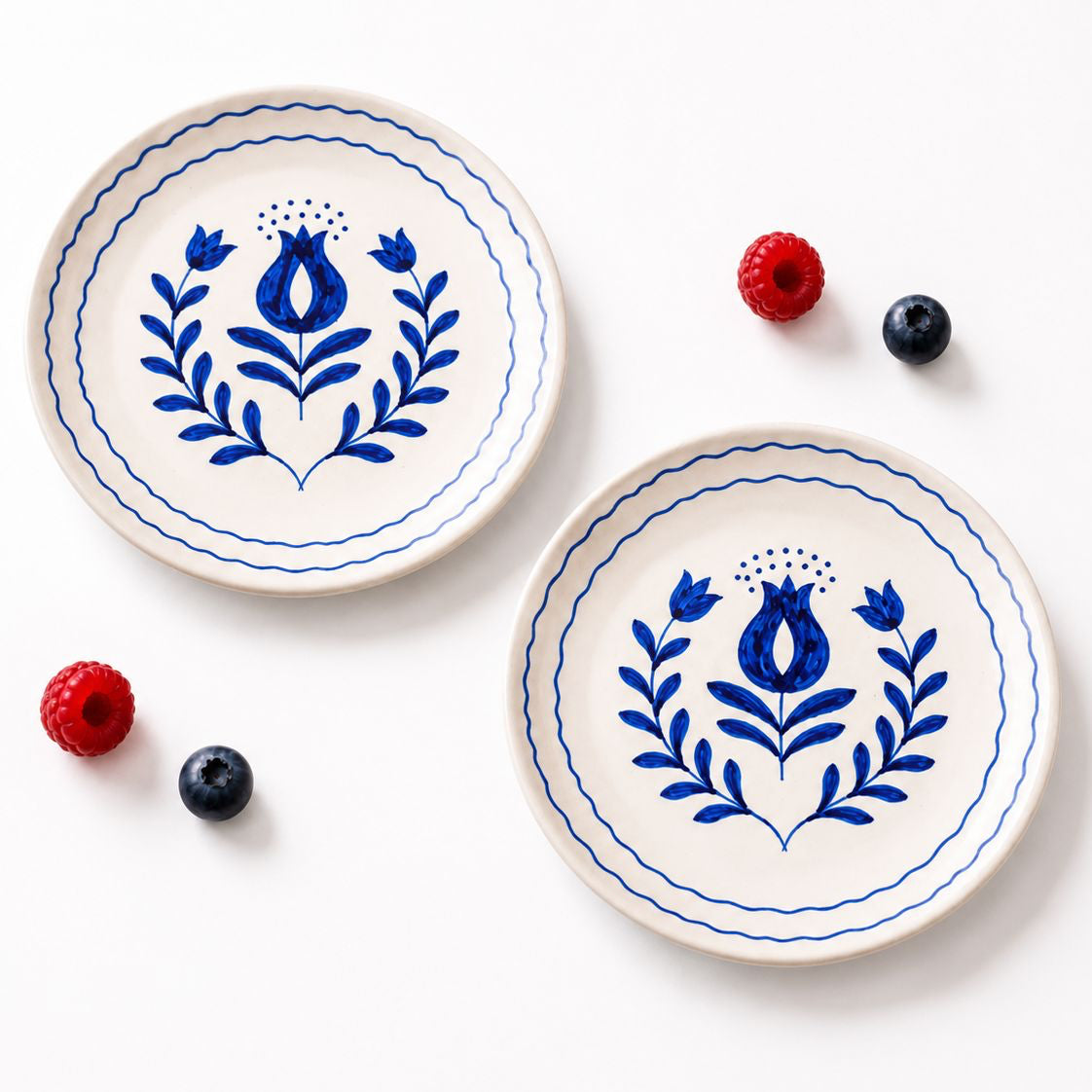 Two ceramic plates with blue floral designs on a white background with berries.