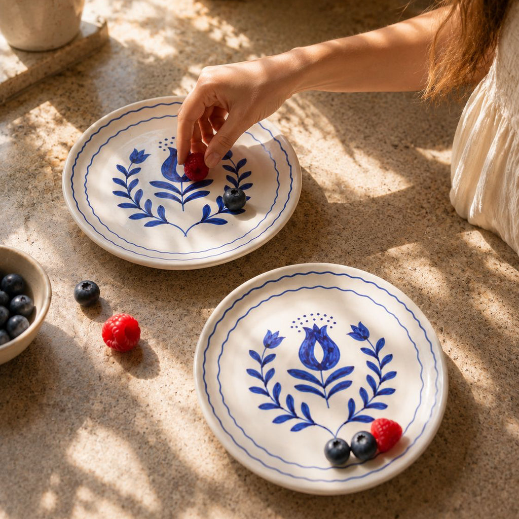 Two ceramic plates with blue floral designs on a sandy surface with berries.