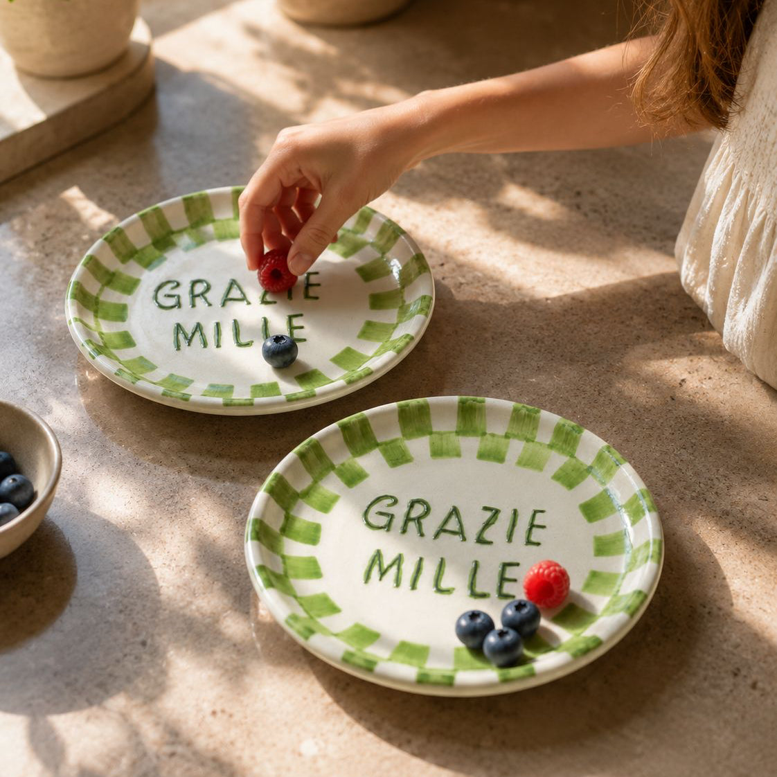 Two small ceramic plates with green checkered rim and 'Grazie Mille' text on a stone surface.