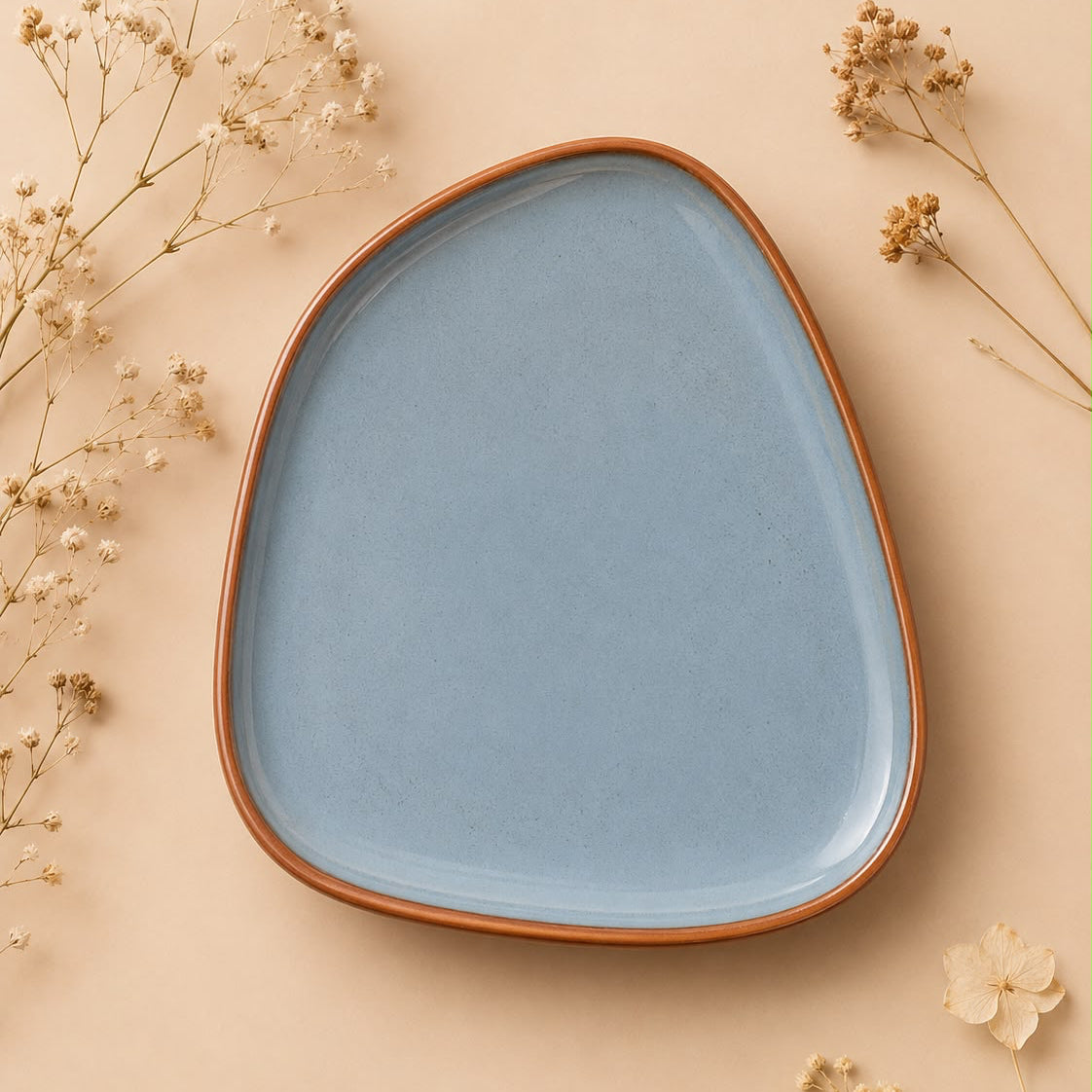Blue ceramic plate with brown rim on a beige background with dried flowers