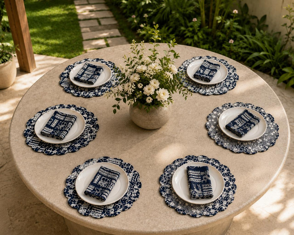 Round table set with white plates, blue and white napkins, and a vase of flowers outdoors.