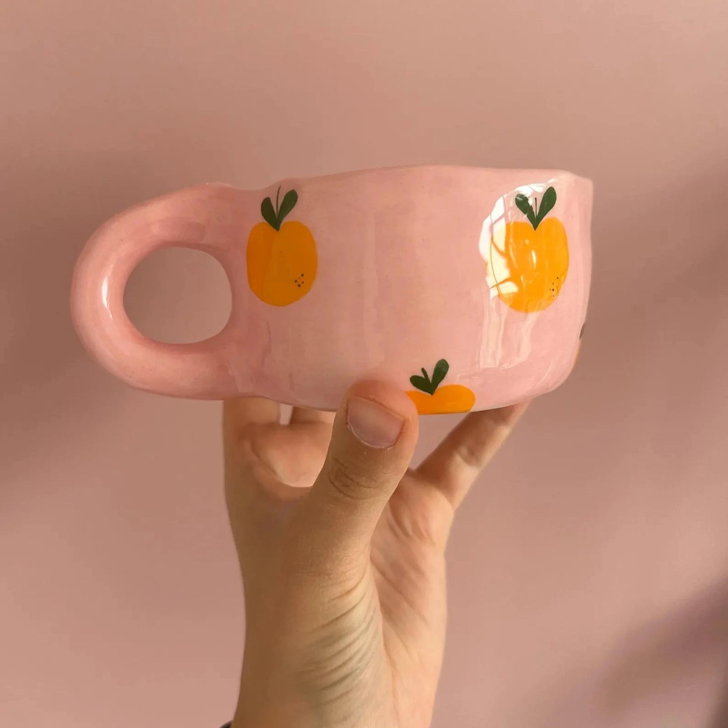 Pink mug with orange designs held against a pink background