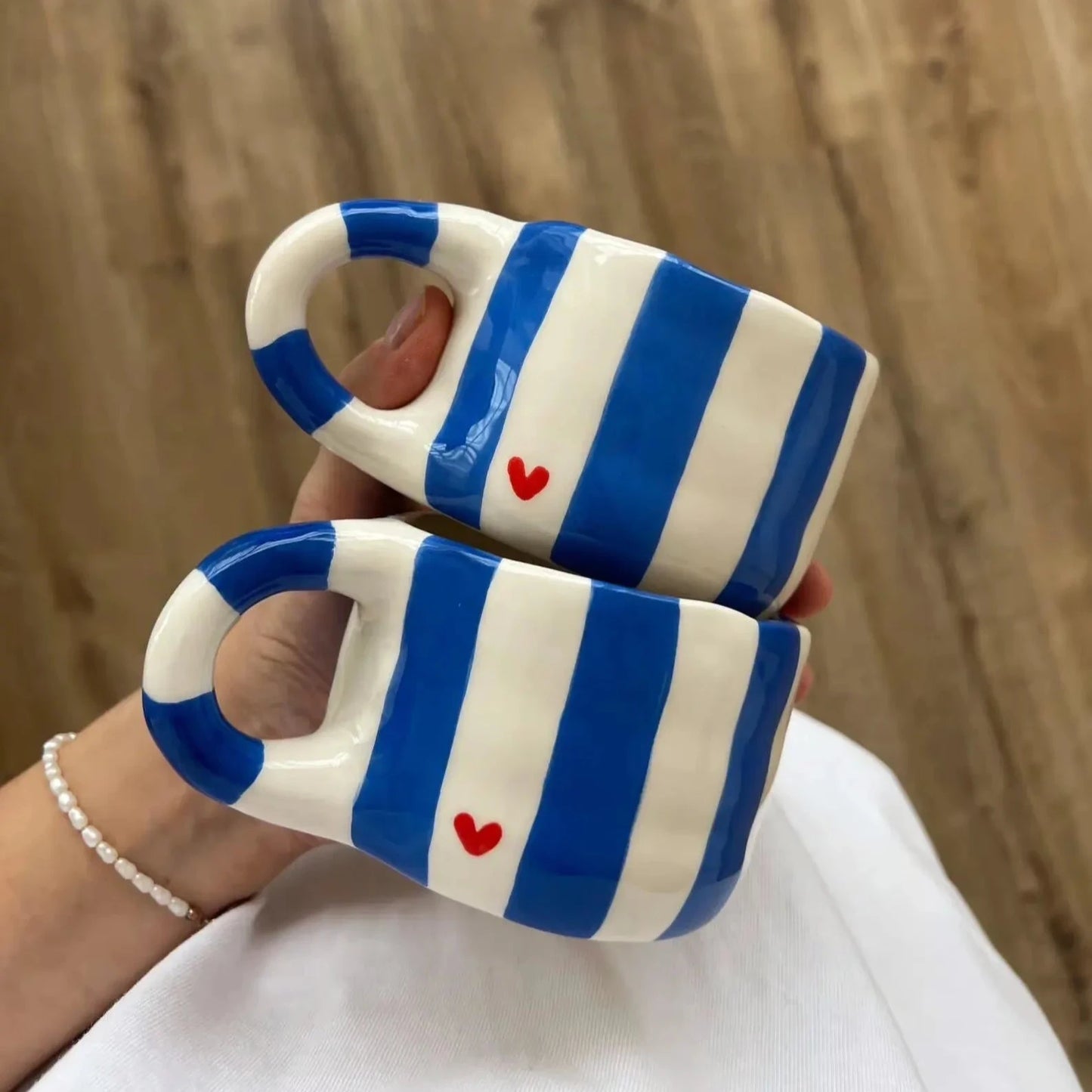 Two blue and white striped ceramic cups with red hearts held against a wooden background.