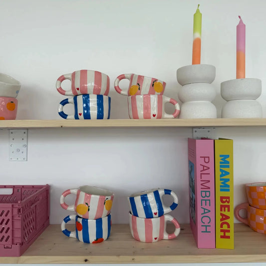Shelves with colorful mugs, books, and candles against a white wall.